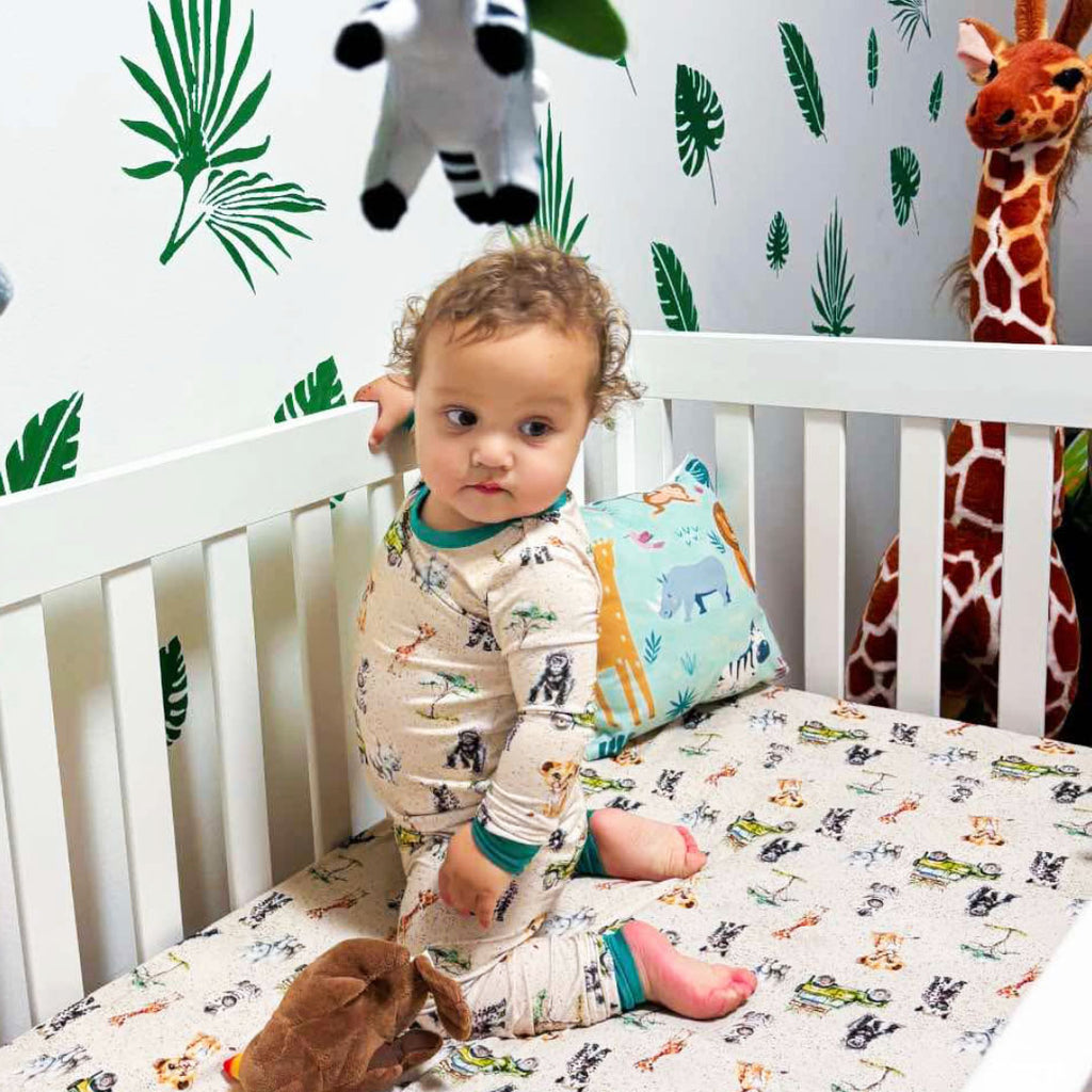 Child in a crib in a safari-themed nursery with safari-themed bamboo pajamas and crib sheet