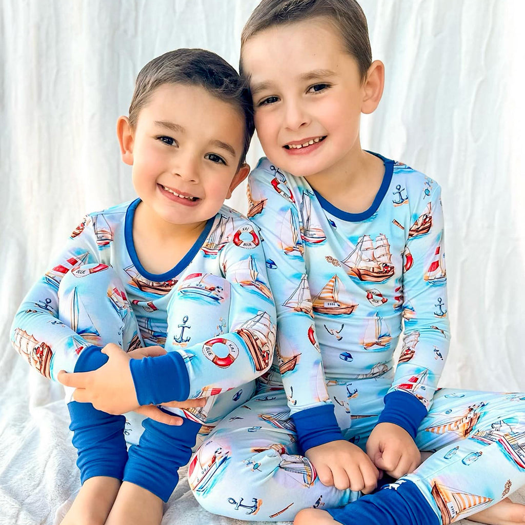 Two children wearing matching pajamas with nautical patterns on a white background