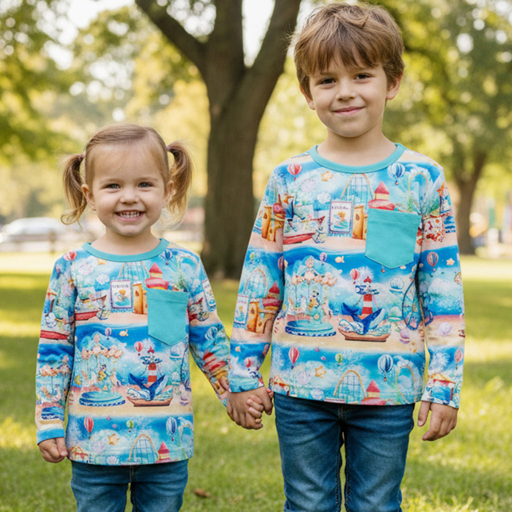 Two children wearing colorful long-sleeve bamboo shirts with n underwater carnival design, standing in a park.