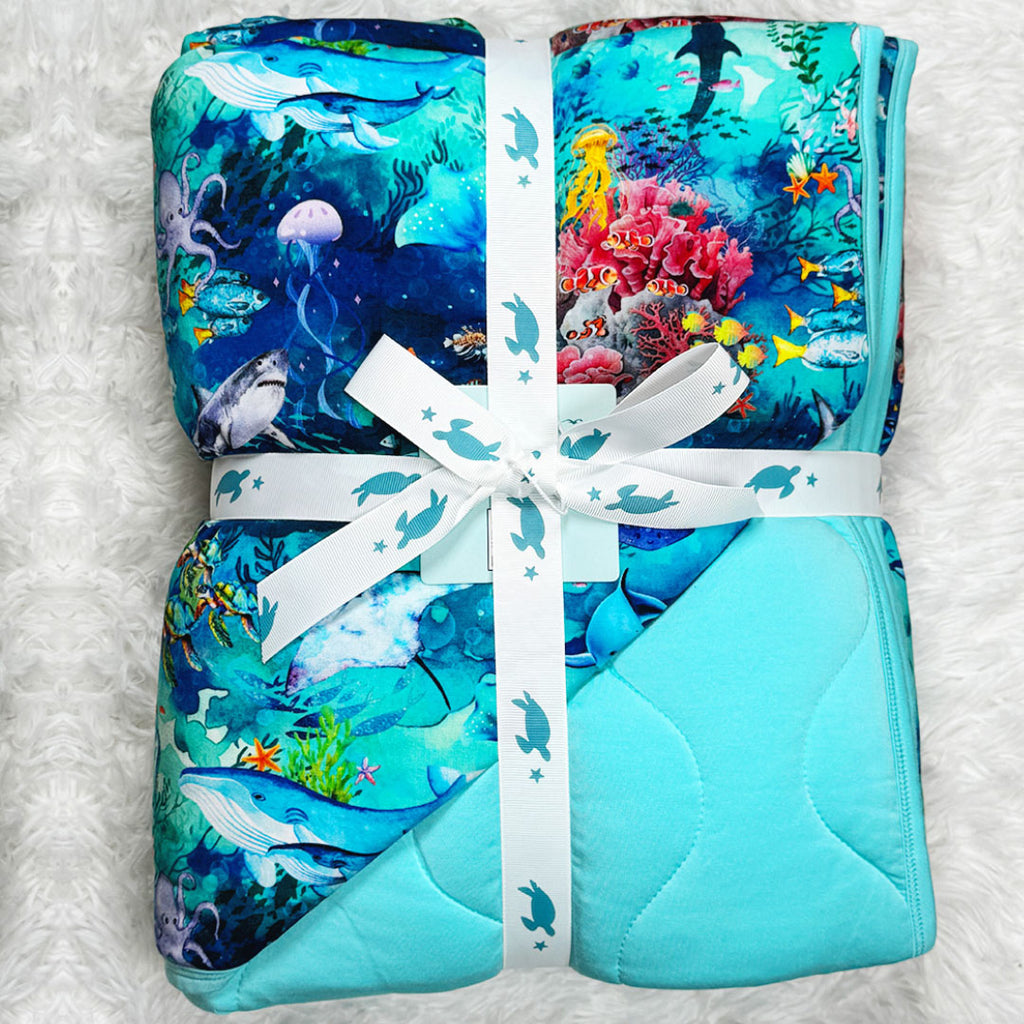Folded quilted bamboo blanket with underwater ocean theme by Kai Blue
