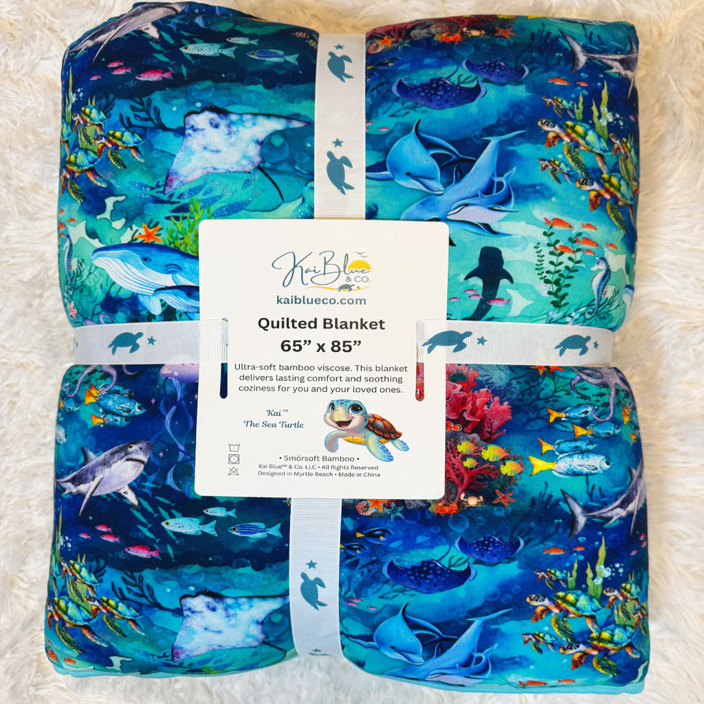 Folded quilted bamboo blanket front view with tag with underwater ocean theme by Kai Blue