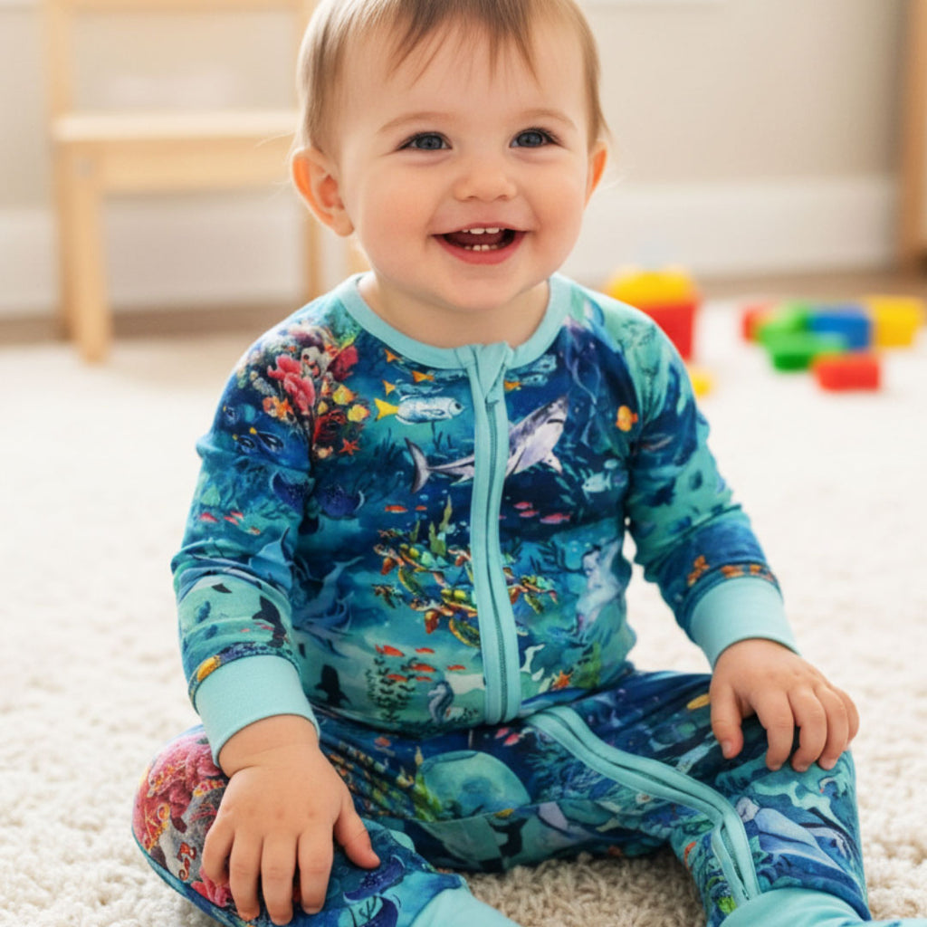 Little boy sitting wearing ocean-themed bamboo zippy by Kai Blue